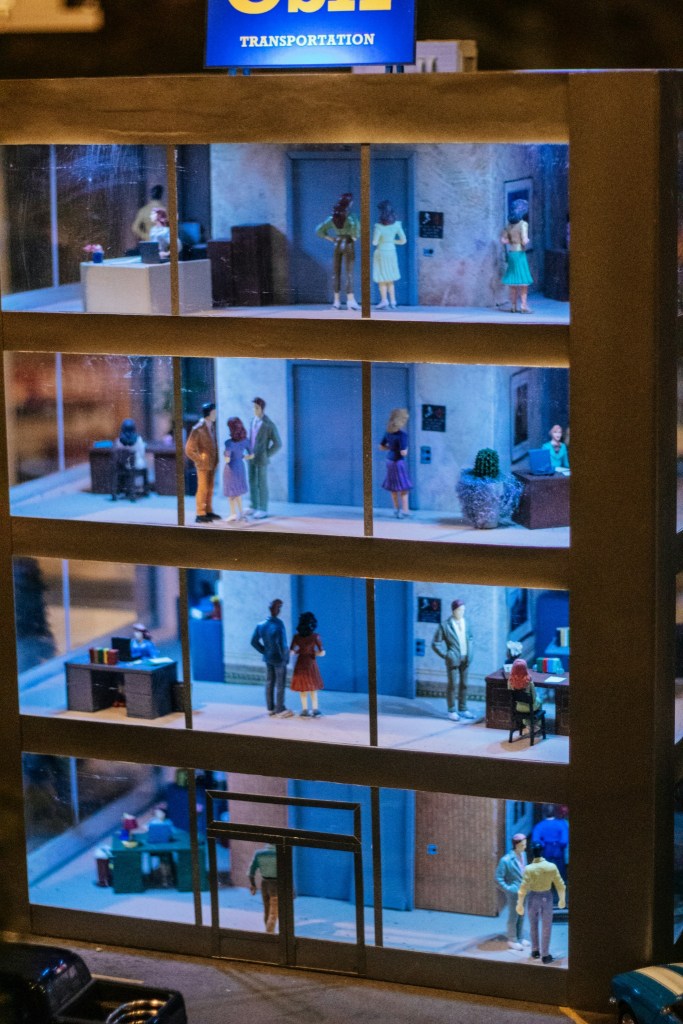 Miniature multi-floor office building representing interconnected teams, customer signals and revenue operations.